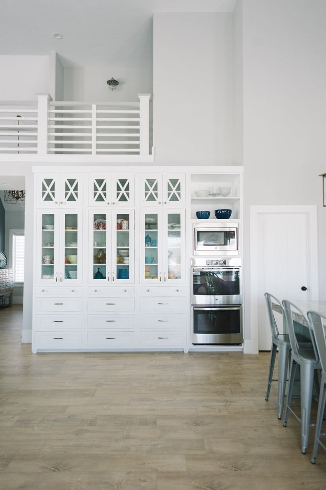 Large beach style single-wall eat-in kitchen in Salt Lake City with with island, shaker cabinets, white cabinets, quartz benchtops, white splashback, porcelain splashback, stainless steel appliances, a farmhouse sink and light hardwood floors.