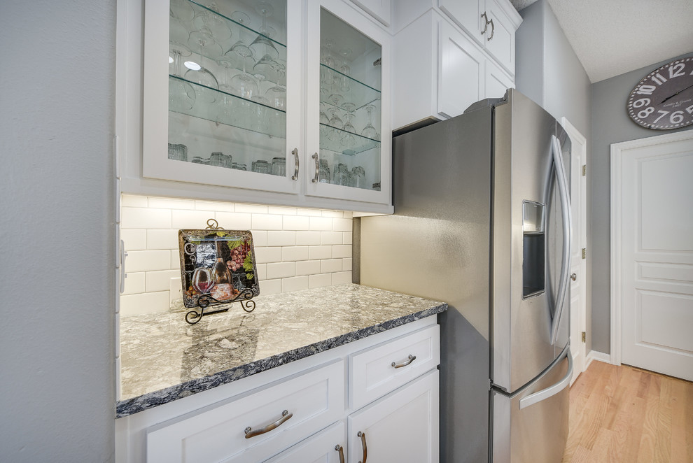 Inspiration for a mid-sized transitional l-shaped light wood floor and brown floor enclosed kitchen remodel in Portland with a drop-in sink, shaker cabinets, white cabinets, quartz countertops, white backsplash, subway tile backsplash, an island and stainless steel appliances