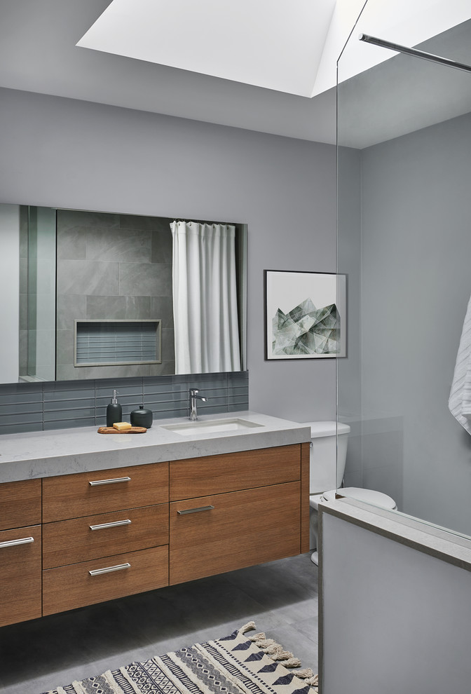 Mid-sized scandinavian kids bathroom in Toronto with flat-panel cabinets, medium wood cabinets, a drop-in tub, a shower/bathtub combo, blue tile, glass tile, ceramic floors, engineered quartz benchtops, a shower curtain and grey benchtops.