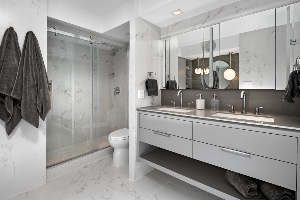 Photo of a mid-sized contemporary master bathroom in Chicago with a sliding shower screen, grey cabinets, an alcove shower, a two-piece toilet, grey walls, marble floors, an undermount sink, solid surface benchtops, grey floor and flat-panel cabinets.