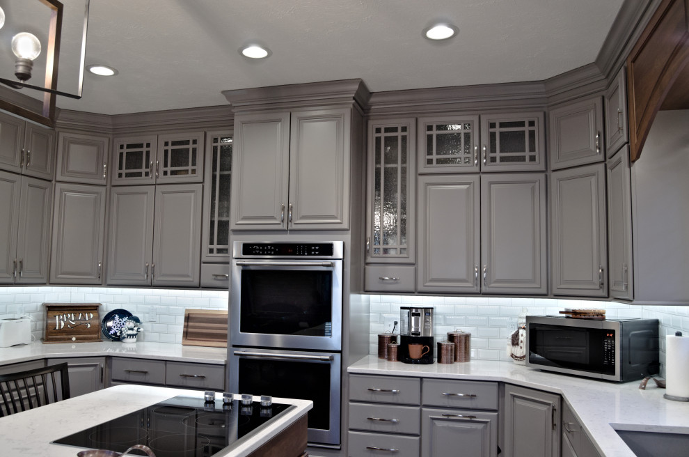Example of an u-shaped brown floor eat-in kitchen design with a double-bowl sink, raised-panel cabinets, gray cabinets, marble countertops, white backsplash, stainless steel appliances, an island and white countertops