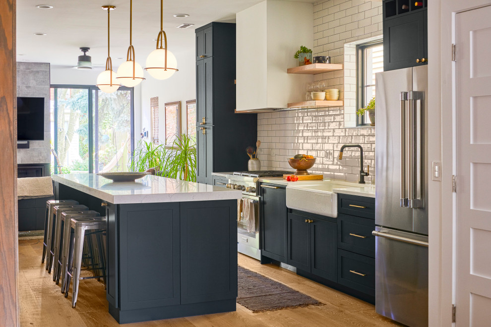 Inspiration for a mid-sized contemporary open plan kitchen in Chicago with subway tile splashback, medium hardwood floors, with island, white benchtop, a drop-in sink, white splashback and black appliances.