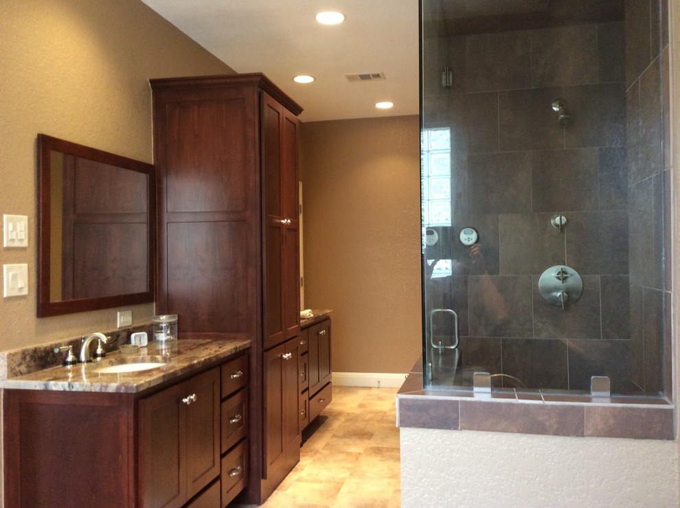 This is an example of a mid-sized transitional master bathroom in Austin with recessed-panel cabinets, dark wood cabinets, a corner shower, stone tile, beige walls, linoleum floors, an undermount sink, granite benchtops, brown floor and a hinged shower door.
