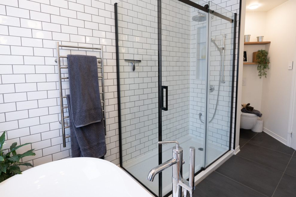 This is an example of a mid-sized modern bathroom in Montreal with flat-panel cabinets, white cabinets, a freestanding tub, a corner shower, a wall-mount toilet, white tile, ceramic tile, grey walls, porcelain floors, a vessel sink, wood benchtops, black floor, a sliding shower screen, a niche, a single vanity, a built-in vanity and planked wall panelling.