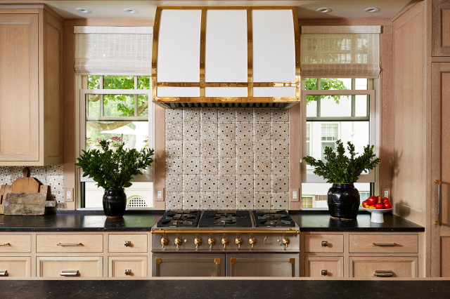 Stacked brown kitchen cabinets flank a black range hood mounted to white  subway backsplash tiles over a stai…