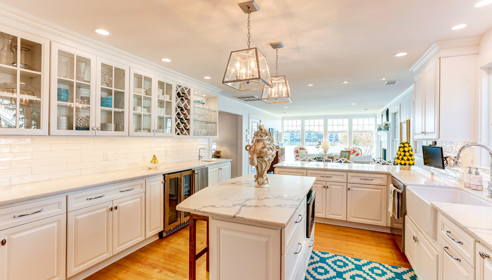 This is an example of a large beach style open plan kitchen in Wilmington with white cabinets, marble benchtops, white splashback, subway tile splashback, stainless steel appliances, light hardwood floors and with island.