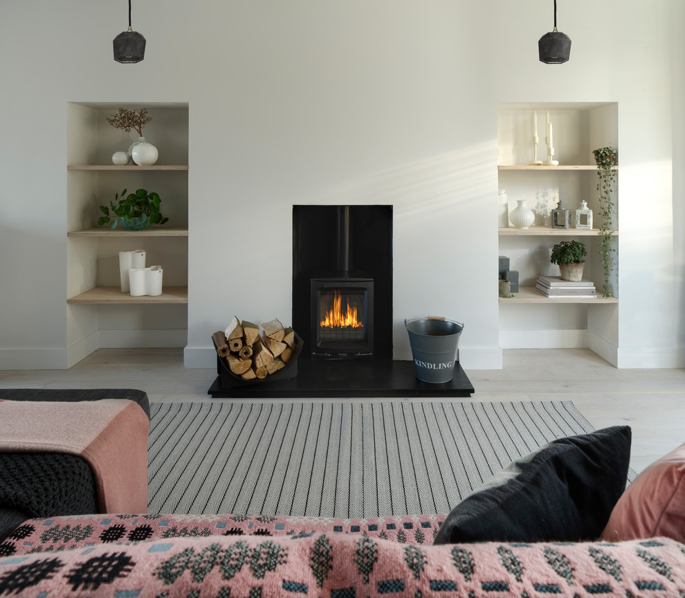 This is an example of a small contemporary open concept living room in Sussex with white walls, light hardwood floors, a wood stove, a plaster fireplace surround and white floor.