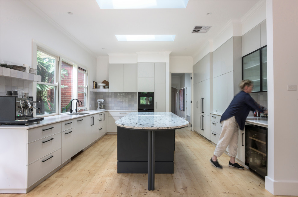 Photo of a large contemporary u-shaped open plan kitchen in Melbourne with a double-bowl sink, beige cabinets, terrazzo worktops, black appliances, light hardwood flooring, an island and multicoloured worktops.