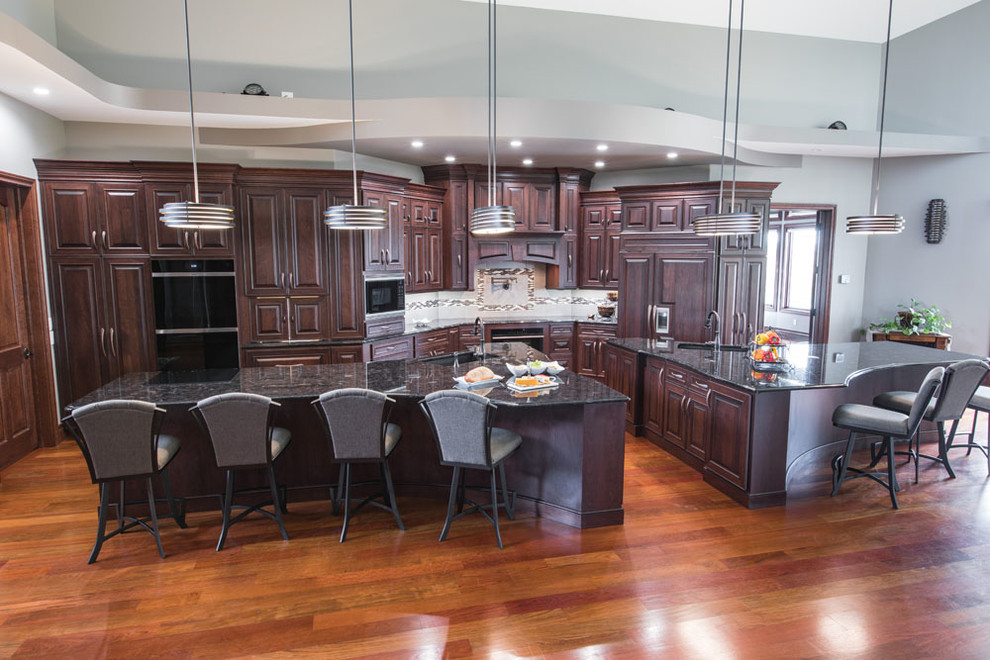 Example of a transitional single-wall medium tone wood floor and brown floor eat-in kitchen design with an undermount sink, raised-panel cabinets, dark wood cabinets, granite countertops, black appliances, two islands and black countertops