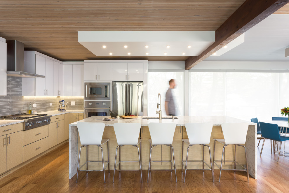 Contemporary l-shaped eat-in kitchen in Chicago with an undermount sink, flat-panel cabinets, white cabinets, grey splashback, matchstick tile splashback, stainless steel appliances, medium hardwood floors and with island.