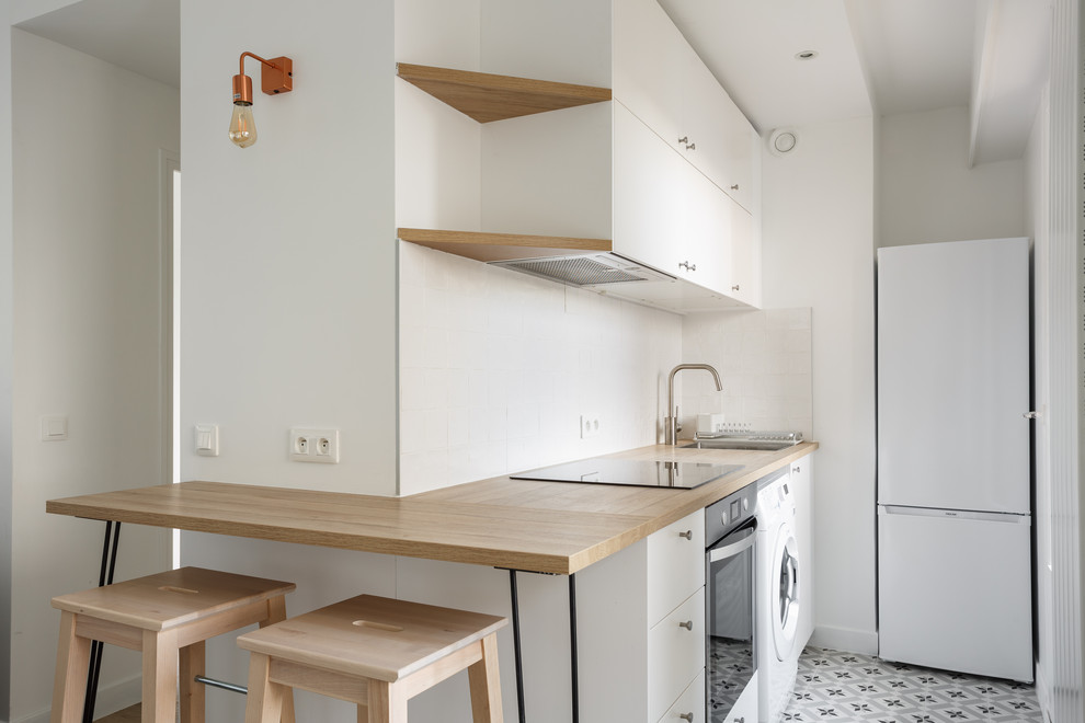 Inspiration for a small scandinavian single-wall open plan kitchen in Other with a single-bowl sink, flat-panel cabinets, white cabinets, wood benchtops, white splashback, ceramic splashback, white appliances, cement tiles, no island, grey floor and beige benchtop.