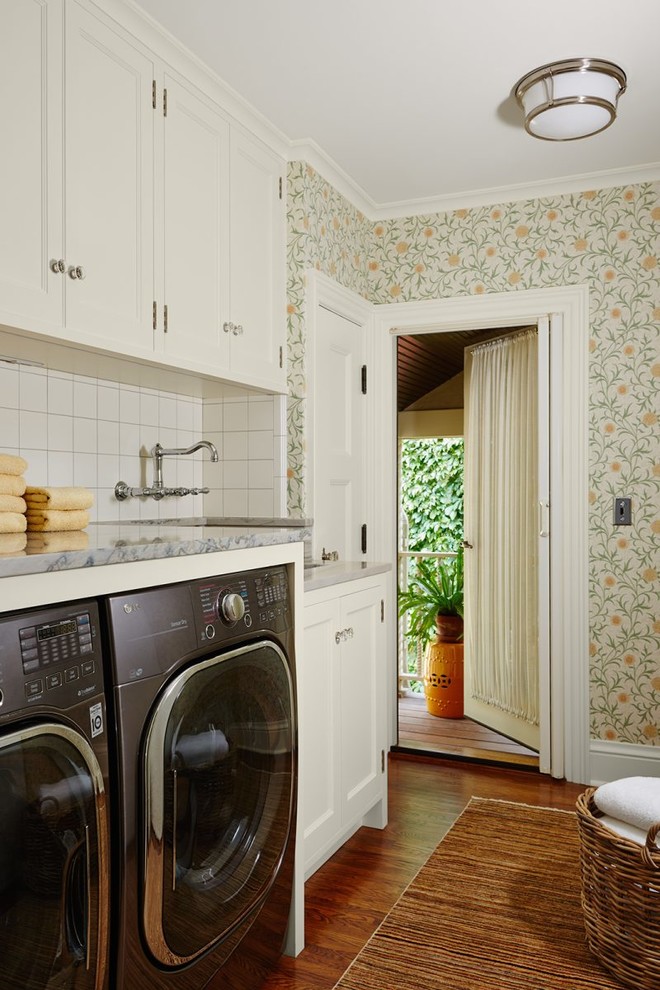 This is an example of a mediterranean single-wall laundry room in Minneapolis with recessed-panel cabinets, white cabinets, multi-coloured walls, medium hardwood floors, a side-by-side washer and dryer, brown floor and grey benchtop.