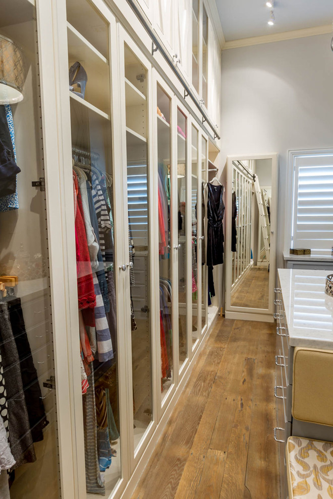 Design ideas for a transitional walk-in wardrobe in Los Angeles with white cabinets and glass-front cabinets.