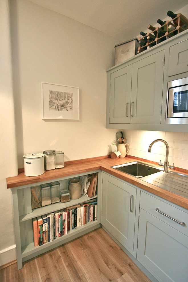 Photo of a small contemporary galley eat-in kitchen in London with a drop-in sink, shaker cabinets, wood benchtops, white splashback, ceramic splashback, stainless steel appliances, medium hardwood floors, no island and blue cabinets.