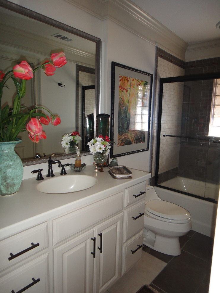 This is an example of a small eclectic kids bathroom in Little Rock with raised-panel cabinets, beige cabinets, an alcove tub, a shower/bathtub combo, a one-piece toilet, brown tile, porcelain tile, beige walls, porcelain floors, an integrated sink and solid surface benchtops.