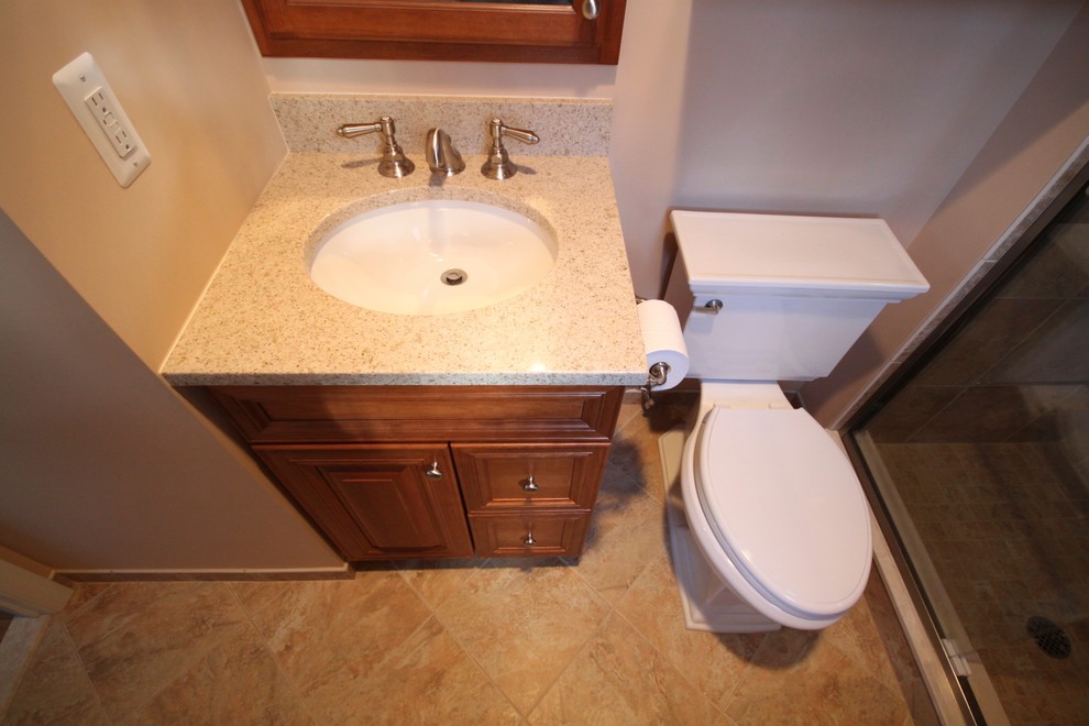 This is an example of a traditional bathroom in New York with an integrated sink, raised-panel cabinets, marble benchtops, an alcove shower, a two-piece toilet and beige tile.