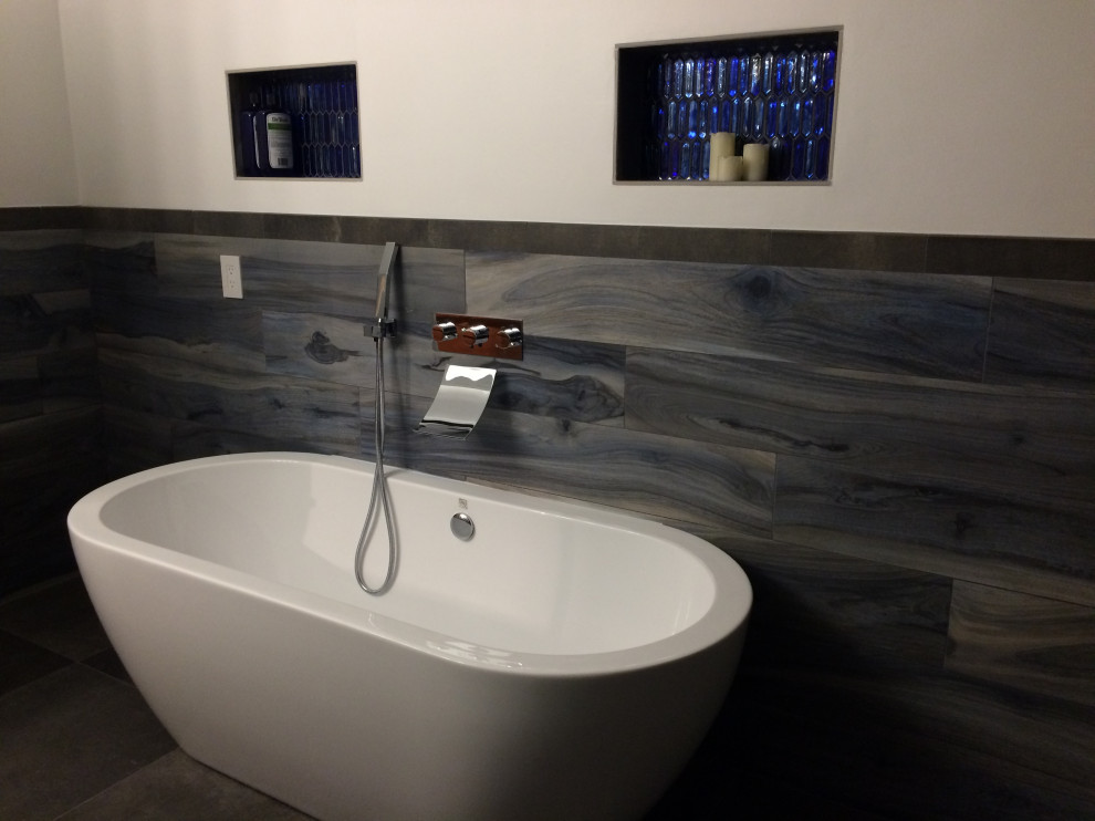 This is an example of a mid-sized modern master bathroom in Orange County with flat-panel cabinets, medium wood cabinets, a freestanding tub, a curbless shower, a wall-mount toilet, blue tile, ceramic tile, white walls, ceramic floors, an integrated sink, engineered quartz benchtops, grey floor, an open shower, white benchtops, a niche, a double vanity, a floating vanity and decorative wall panelling.