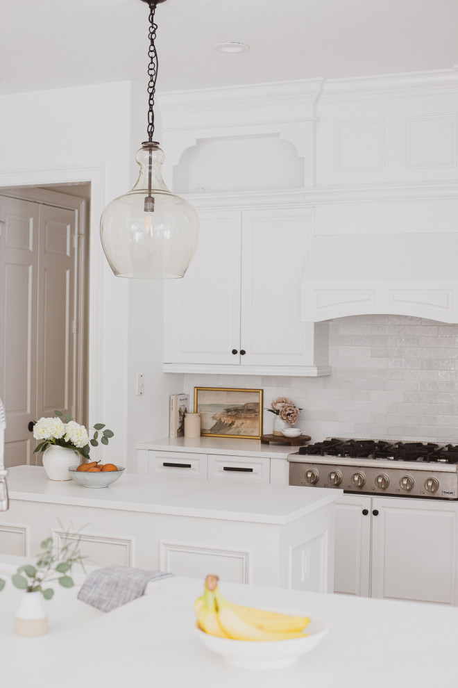 Inspiration for a mid-sized transitional u-shaped eat-in kitchen in Orlando with a drop-in sink, shaker cabinets, white cabinets, quartz benchtops, white splashback, ceramic splashback, stainless steel appliances, travertine floors, with island, brown floor and white benchtop.