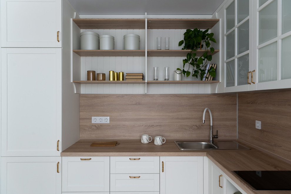 Photo of a medium sized classic l-shaped kitchen/diner in Other with a submerged sink, raised-panel cabinets, white cabinets, laminate countertops, brown splashback, wood splashback, stainless steel appliances, medium hardwood flooring, no island, beige floors and brown worktops.