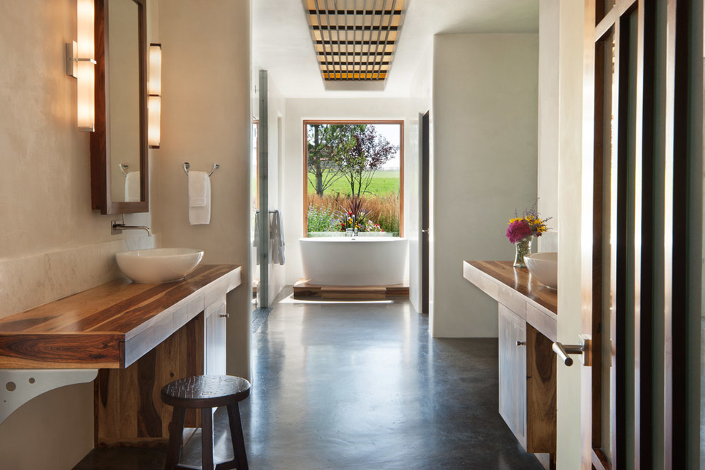 Inspiration for a large asian master bathroom in Denver with a vessel sink, wood benchtops, a freestanding tub, beige walls, light wood cabinets, a double shower, a two-piece toilet, concrete floors, grey floor, a hinged shower door, white tile, brown benchtops and flat-panel cabinets.