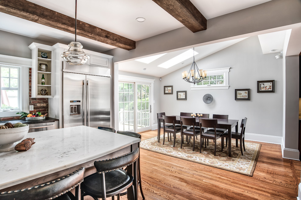 This is an example of a large country eat-in kitchen in New York with beaded inset cabinets, white cabinets, brick splashback, stainless steel appliances, with island, brown floor, a farmhouse sink, granite benchtops, painted wood floors and white benchtop.
