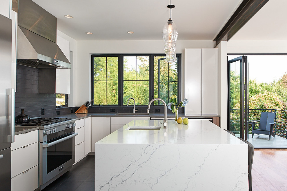 This is an example of a contemporary l-shaped eat-in kitchen in Seattle with with island, an undermount sink, flat-panel cabinets, white cabinets, grey splashback, stainless steel appliances, grey floor and white benchtop.