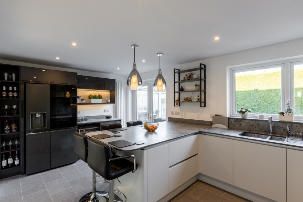 Medium sized contemporary u-shaped open plan kitchen in Sussex with flat-panel cabinets, grey cabinets, quartz worktops, grey splashback, engineered quartz splashback, black appliances and grey worktops.