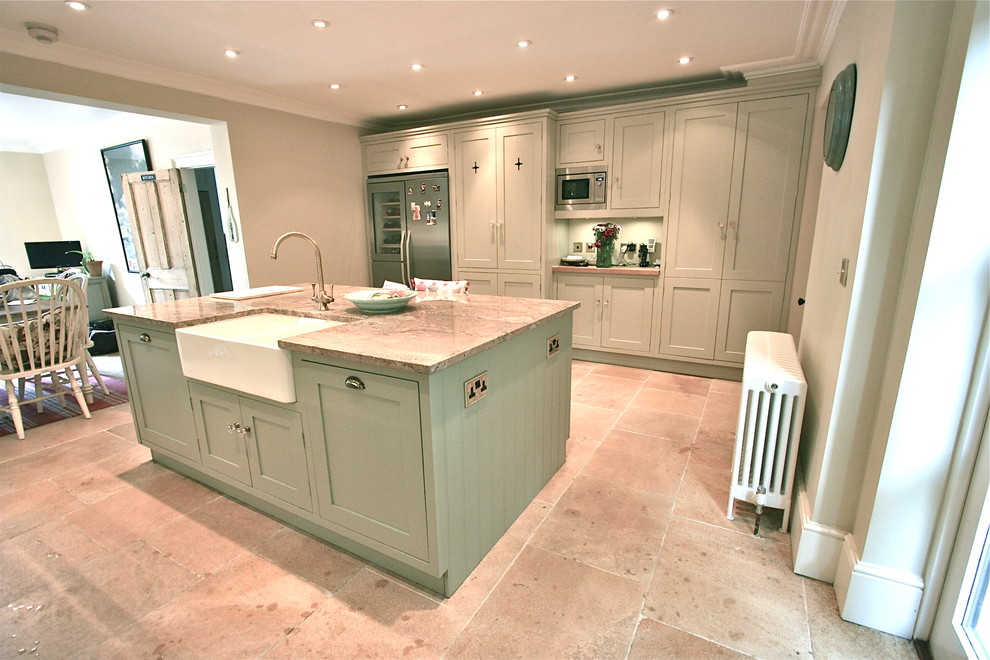 This is an example of a large traditional kitchen in London with a farmhouse sink, shaker cabinets, green cabinets, granite benchtops, coloured appliances, travertine floors and with island.