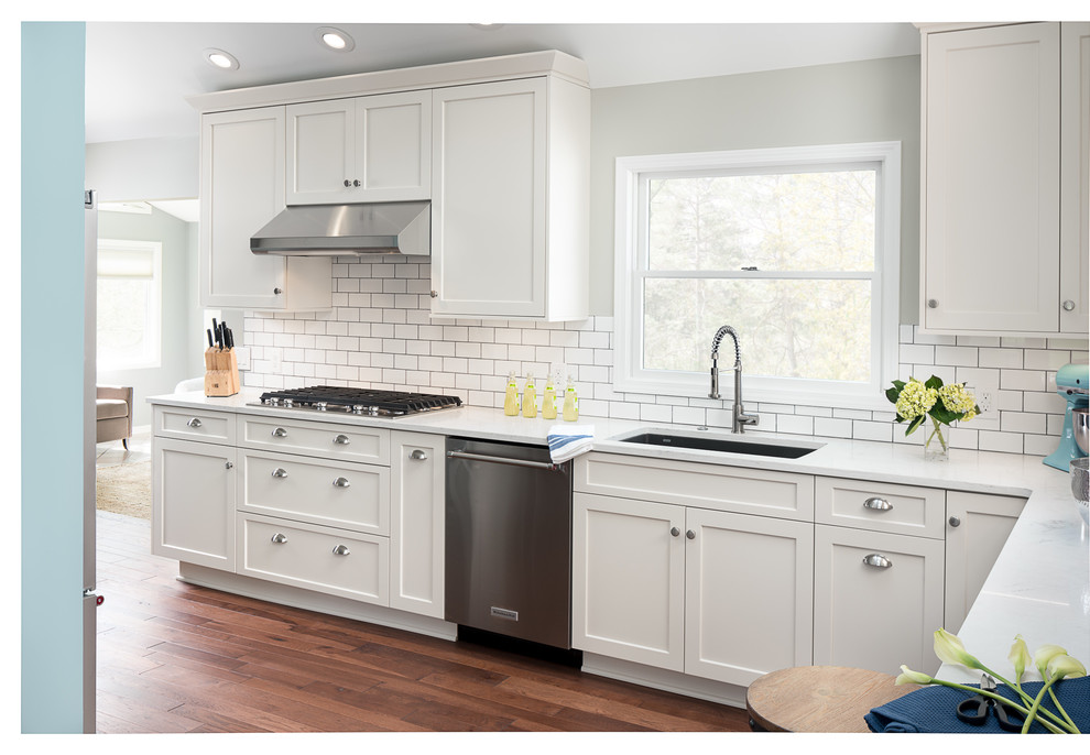 Example of a large transitional l-shaped medium tone wood floor kitchen design in New York with an undermount sink, flat-panel cabinets, blue cabinets, quartz countertops, white backsplash, ceramic backsplash, stainless steel appliances and a peninsula