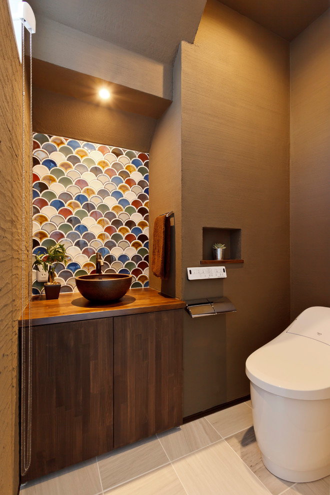 Photo of an asian powder room in Other with dark wood cabinets, a one-piece toilet, multi-coloured tile, brown walls, wood benchtops, beige floor and brown benchtops.