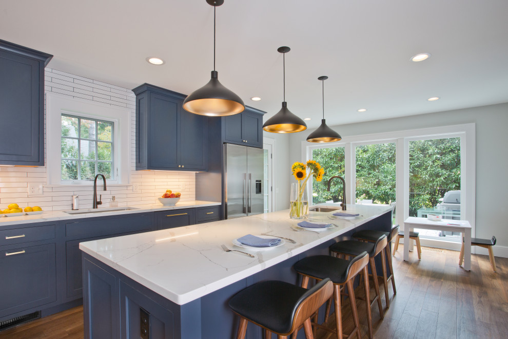 This is an example of a mid-sized transitional kitchen in New York with blue cabinets, quartz benchtops, white splashback, ceramic splashback, stainless steel appliances, medium hardwood floors, with island, brown floor, white benchtop, an undermount sink and shaker cabinets.