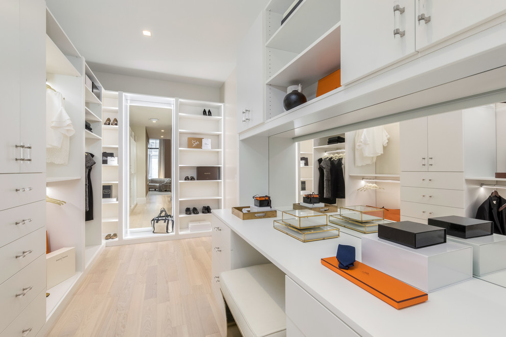 Photo of a large contemporary women's walk-in wardrobe in New York with flat-panel cabinets, white cabinets, light hardwood floors and beige floor.