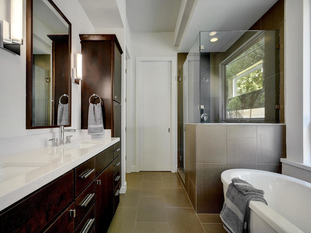 This is an example of a mid-sized contemporary master bathroom in Austin with flat-panel cabinets, dark wood cabinets, a freestanding tub, a corner shower, brown tile, porcelain tile, white walls, porcelain floors, an undermount sink, engineered quartz benchtops, brown floor, a hinged shower door and white benchtops.