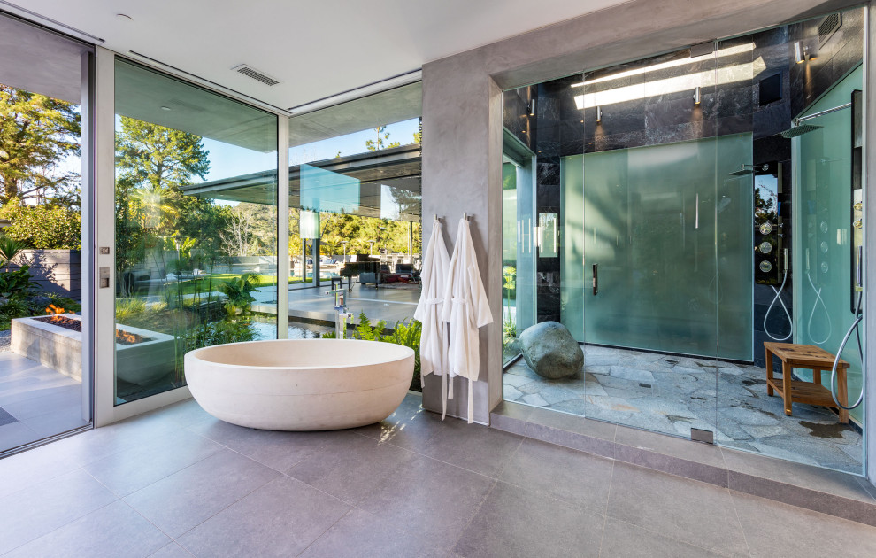 Trendy master ceramic tile and gray floor freestanding bathtub photo in Los Angeles with gray walls and a hinged shower door