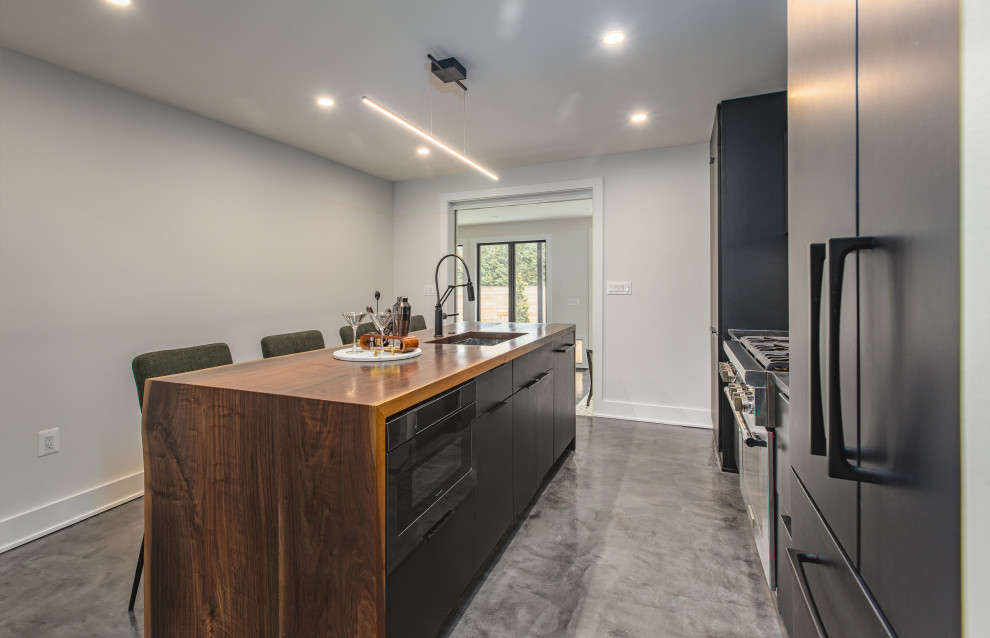 Design ideas for a medium sized urban galley kitchen/diner in DC Metro with a submerged sink, flat-panel cabinets, black cabinets, soapstone worktops, black splashback, stone slab splashback, integrated appliances, concrete flooring, an island, grey floors and black worktops.