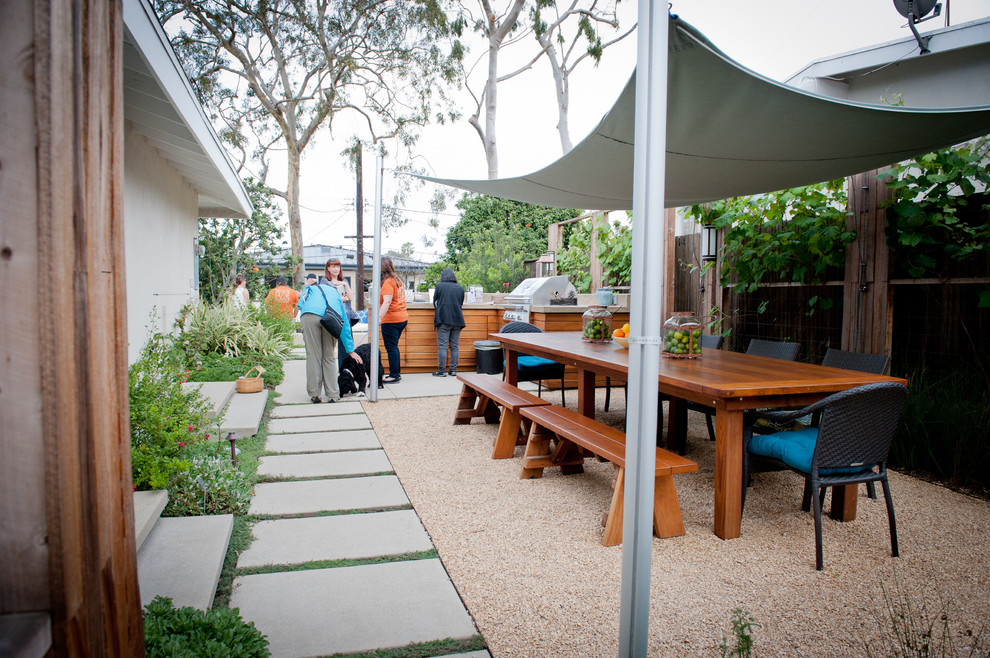 Photo of a large modern side yard patio in Los Angeles with gravel, an outdoor kitchen and an awning.