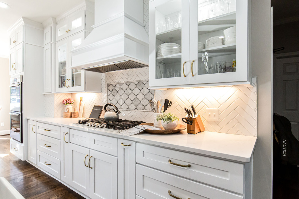 Klassisk inredning av ett stort vit vitt kök, med en rustik diskho, skåp i shakerstil, vita skåp, bänkskiva i kvarts, vitt stänkskydd, stänkskydd i tunnelbanekakel, rostfria vitvaror, mellanmörkt trägolv, en köksö och brunt golv