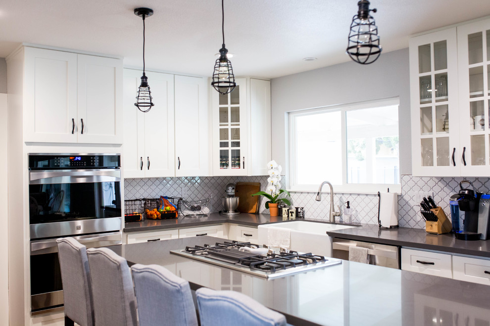 Inspiration for a mid-sized transitional light wood floor eat-in kitchen remodel in Sacramento with a farmhouse sink, shaker cabinets, white cabinets, white backsplash, glass tile backsplash, stainless steel appliances and an island