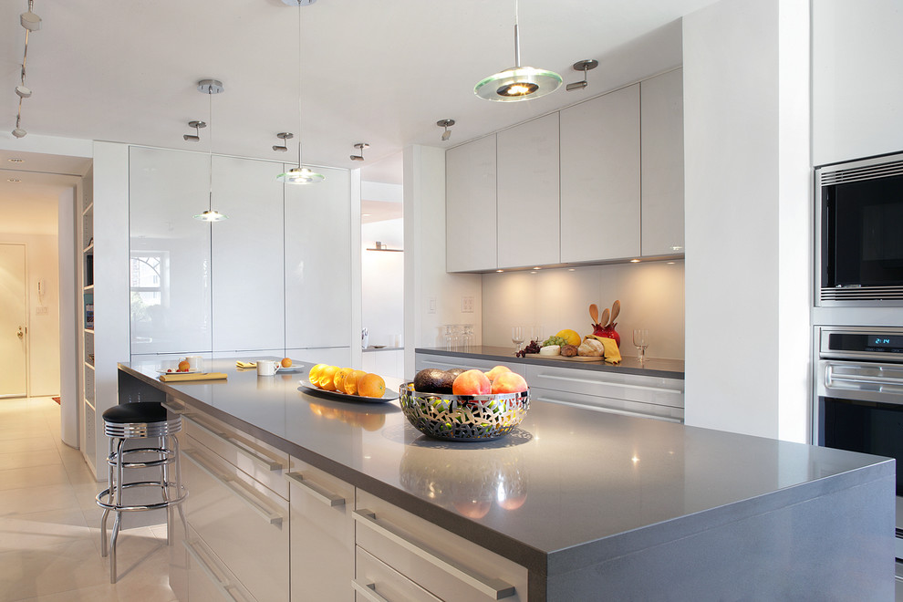 Mid-sized modern eat-in kitchen in New York with quartz benchtops, grey splashback, glass sheet splashback, stainless steel appliances, an undermount sink, flat-panel cabinets, stainless steel cabinets, porcelain floors and with island.