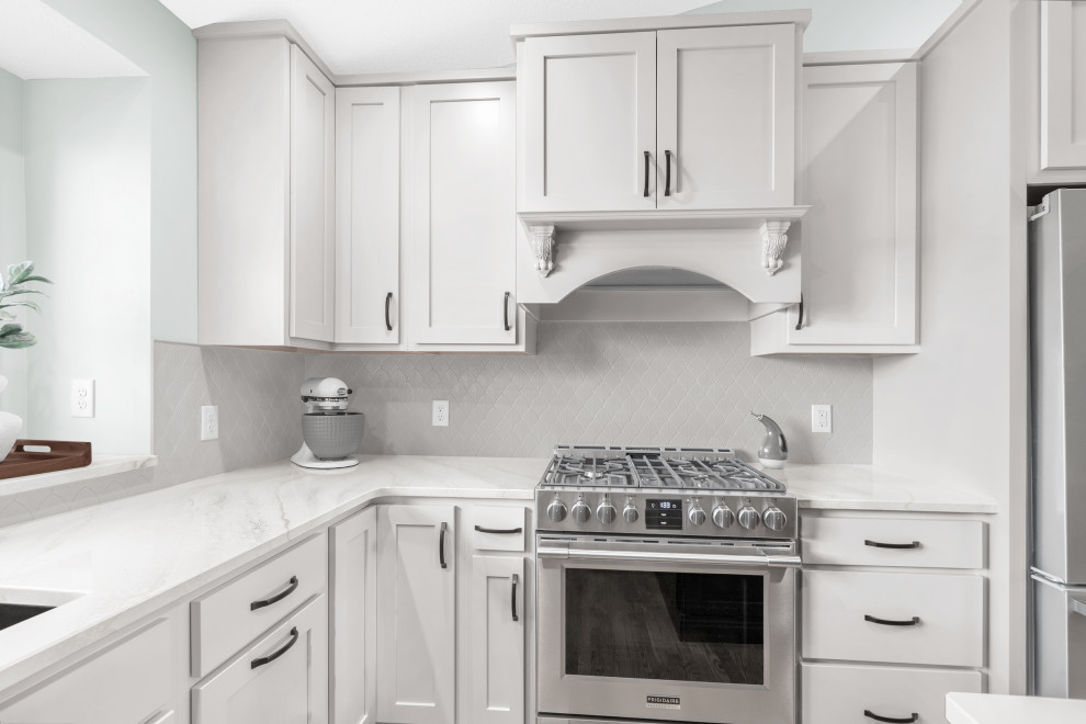 Example of a mid-sized transitional l-shaped light wood floor and beige floor kitchen design in Minneapolis with an undermount sink, shaker cabinets, white cabinets, quartz countertops, white backsplash, ceramic backsplash, stainless steel appliances, an island and white countertops