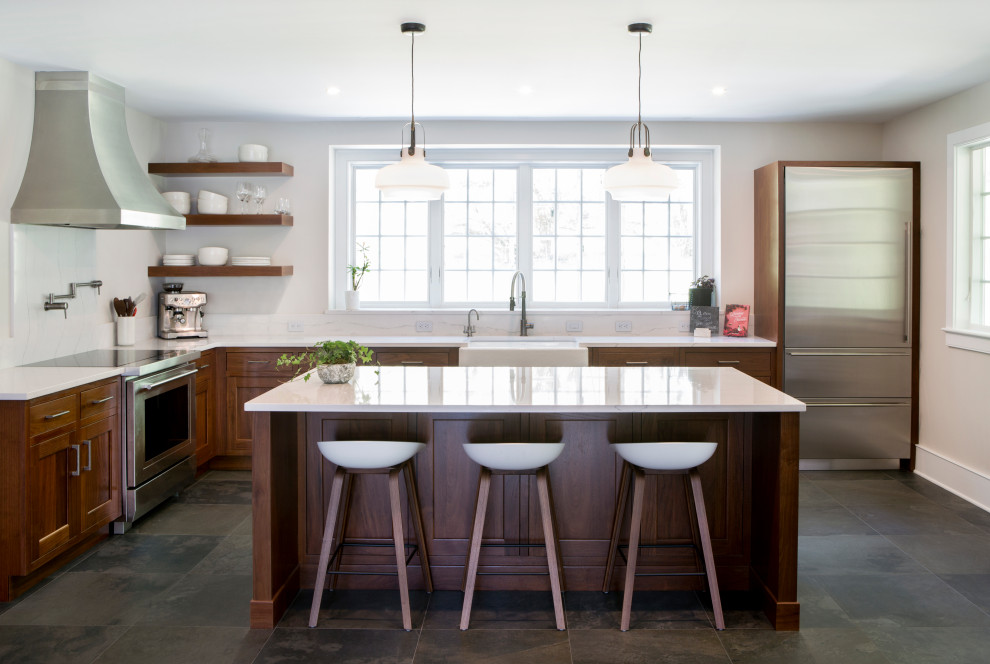 Photo of a mid-sized country u-shaped eat-in kitchen in New York with a farmhouse sink, recessed-panel cabinets, medium wood cabinets, quartz benchtops, white splashback, engineered quartz splashback, stainless steel appliances, porcelain floors, with island, grey floor and white benchtop.