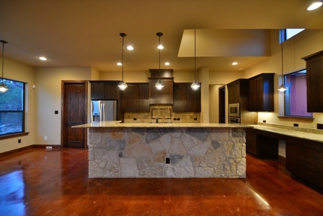 Mid-sized contemporary l-shaped eat-in kitchen in Austin with concrete floors, with island, recessed-panel cabinets, dark wood cabinets, granite benchtops, beige splashback, ceramic splashback and stainless steel appliances.