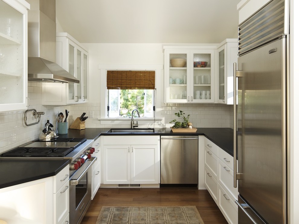 Photo of a contemporary u-shaped separate kitchen in Los Angeles with glass-front cabinets, stainless steel appliances, an undermount sink, white cabinets, white splashback and subway tile splashback.