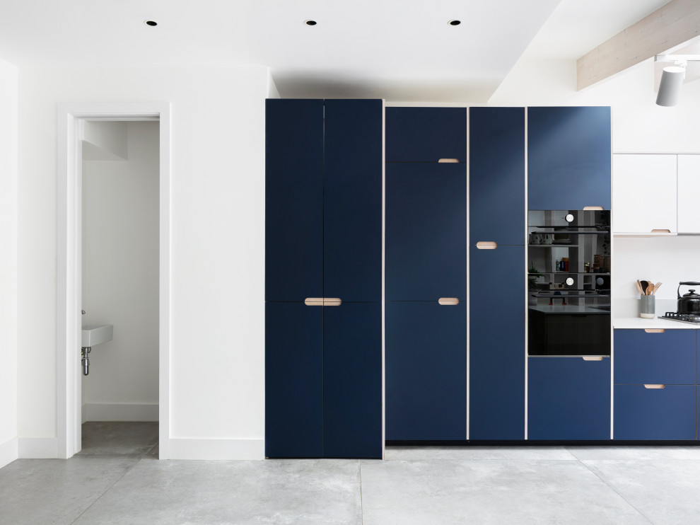 Inspiration for a mid-sized scandinavian galley open plan kitchen in London with a drop-in sink, flat-panel cabinets, blue cabinets, solid surface benchtops, white splashback, granite splashback, black appliances, porcelain floors, no island, grey floor, white benchtop and exposed beam.