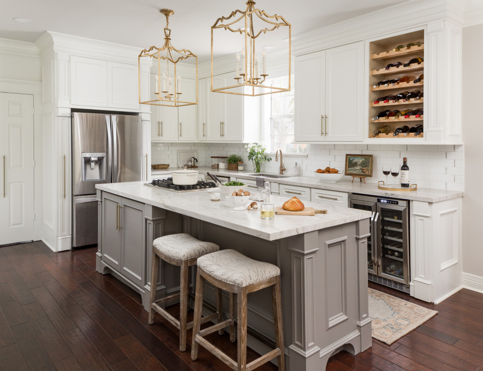 Photo of a traditional l-shaped eat-in kitchen in Houston with an undermount sink, recessed-panel cabinets, white cabinets, white splashback, subway tile splashback, stainless steel appliances, medium hardwood floors, with island, brown floor and grey benchtop.