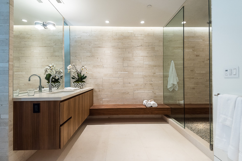 Photo of a mid-sized modern 3/4 bathroom in Los Angeles with flat-panel cabinets, dark wood cabinets, an open shower, a one-piece toilet, beige tile, stone tile, beige walls, limestone floors, an undermount sink and marble benchtops.