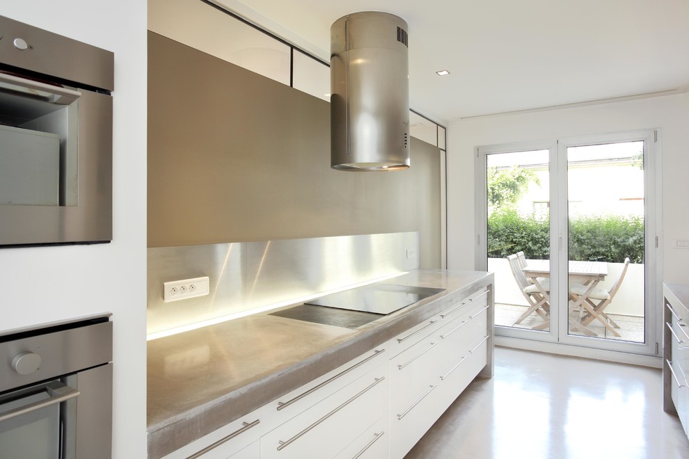 Photo of a contemporary kitchen in Paris with concrete benchtops, metal splashback, stainless steel appliances and concrete floors.