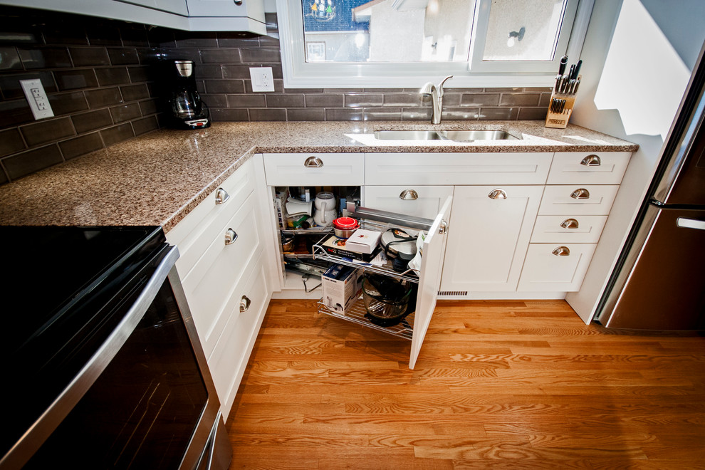 Mid-sized transitional l-shaped light wood floor eat-in kitchen photo with a double-bowl sink, shaker cabinets, white cabinets, quartz countertops, brown backsplash, ceramic backsplash, stainless steel appliances and an island