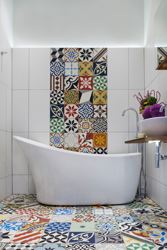 Design ideas for a mediterranean master bathroom in London with a vessel sink, wood benchtops, a freestanding tub, multi-coloured tile, stone tile, multi-coloured walls, multi-coloured floor and brown benchtops.