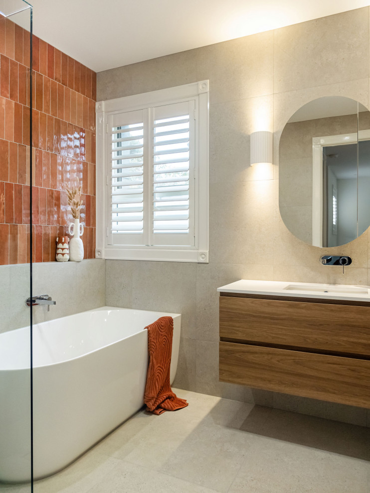 This is an example of a mid-sized contemporary bathroom in Melbourne with flat-panel cabinets, medium wood cabinets, a corner tub, a corner shower, beige tile, porcelain tile, beige walls, porcelain floors, an undermount sink, engineered quartz benchtops, beige floor, a hinged shower door, white benchtops and a single vanity.